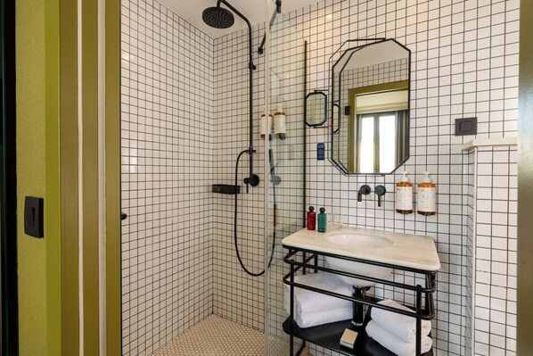 Un baño con ducha, lavamanos, espejo y artículos de aseo.