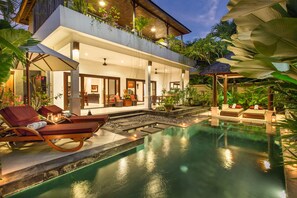 A modern resort with a pool, lounge chairs, and a covered patio area.