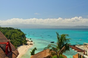 Une plage avec une vue dégagée sur une eau turquoise cristalline, un bâtiment à toit de chaume et un palmier.