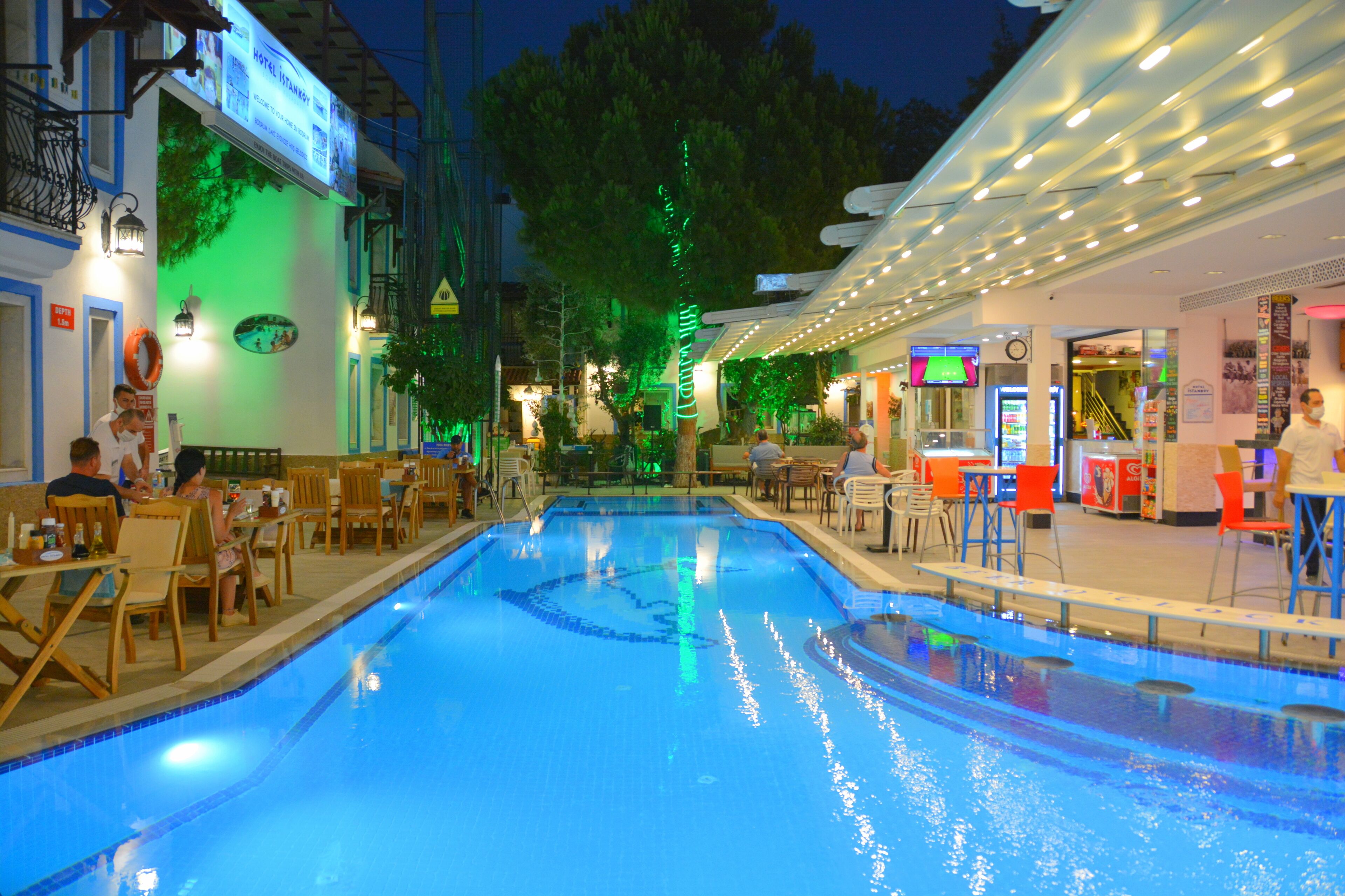 Una piscina rodeada de mesas y sillas, un restaurante y un cartel de hotel.