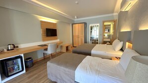 Habitación de hotel con escritorio, dos camas, televisión y minibar.