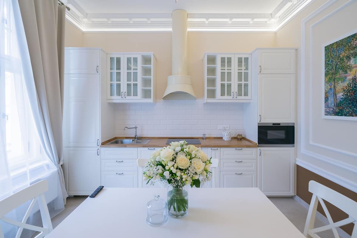 A modern kitchen with white cabinetry, a central island with a vase of flowers, and a microwave.
