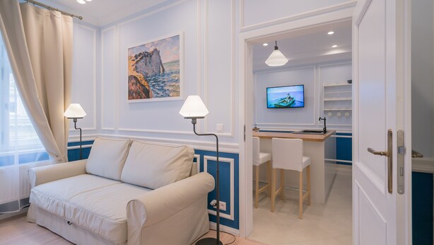 A room with a beige sofa, a desk with a chair, a television, and a painting on the wall.