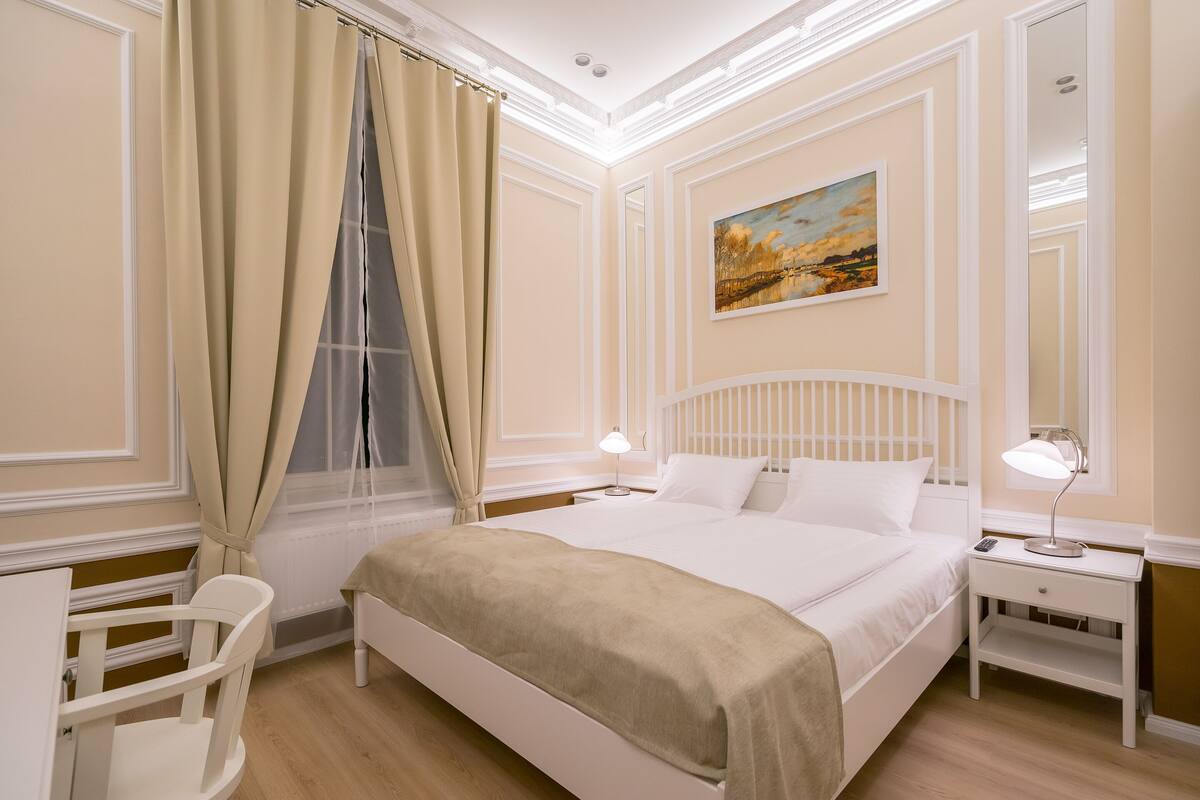 A neatly arranged bedroom with a bed, bedside tables, a chair, and a painting on the wall.