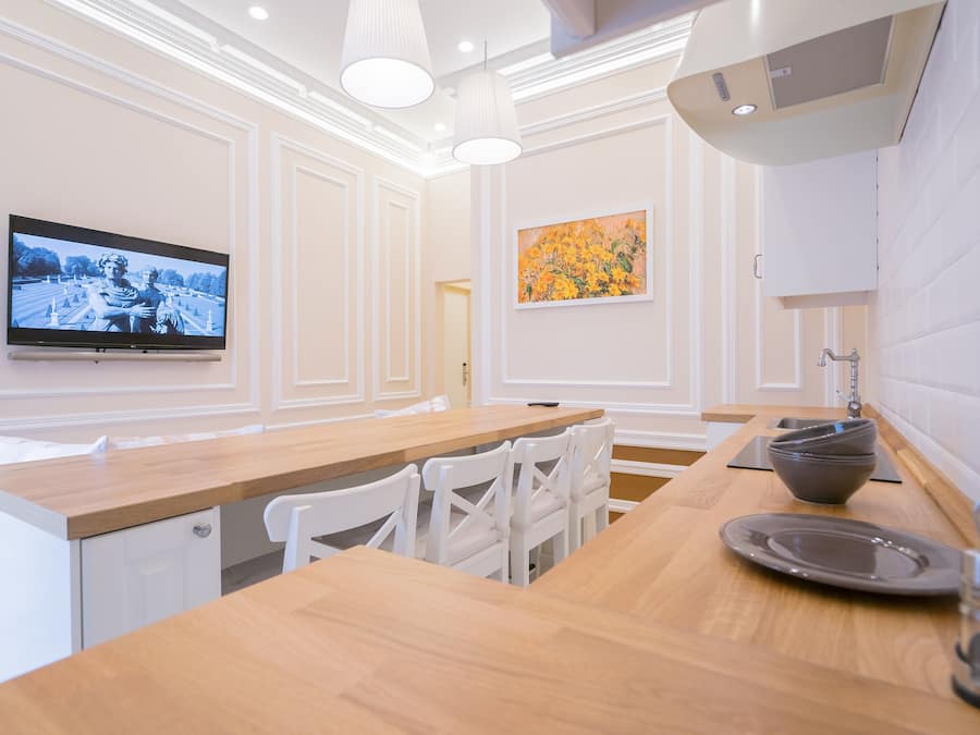 A modern kitchen with white cabinetry, a wooden countertop, and a flat-screen TV mounted on the wall.