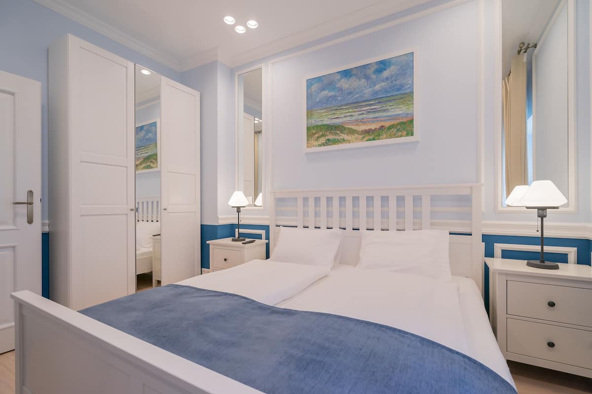 A bedroom with a bed, nightstands, a mirror, and a painting on the wall.