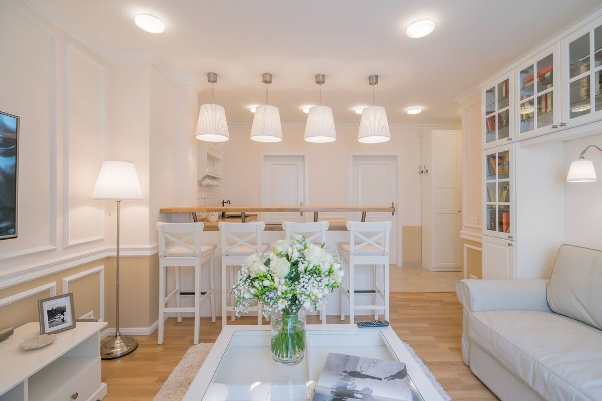A modern living room with a glass coffee table, white sofas, a dining area with chairs, and pendant lights.