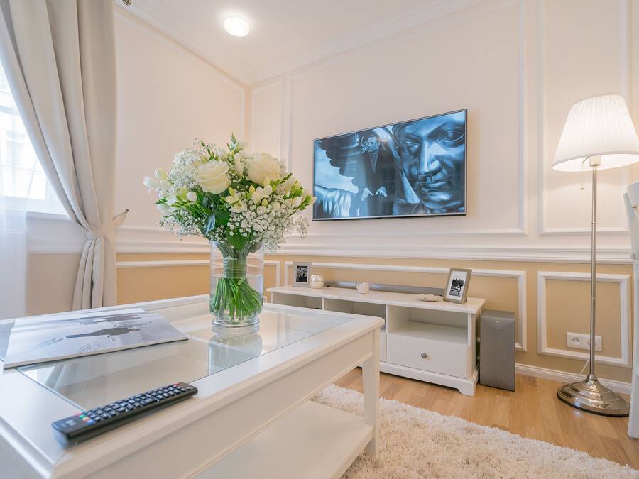A modern living room with a glass coffee table, a remote control, a vase of flowers, a flat-screen TV, and a standing lamp.