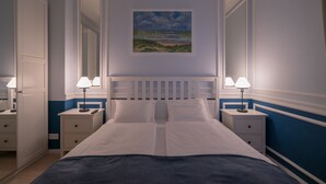 A neatly arranged bedroom with a large bed, two bedside tables with lamps, a painting on the wall, and a mirror above the bed.