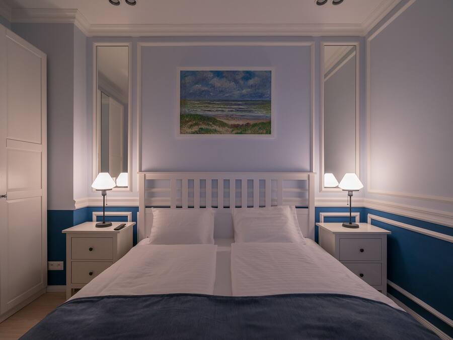 Quarto bem arrumado com uma cama grande, duas mesas de cabeceira com abajures, um quadro na parede e um espelho sobre a cama.