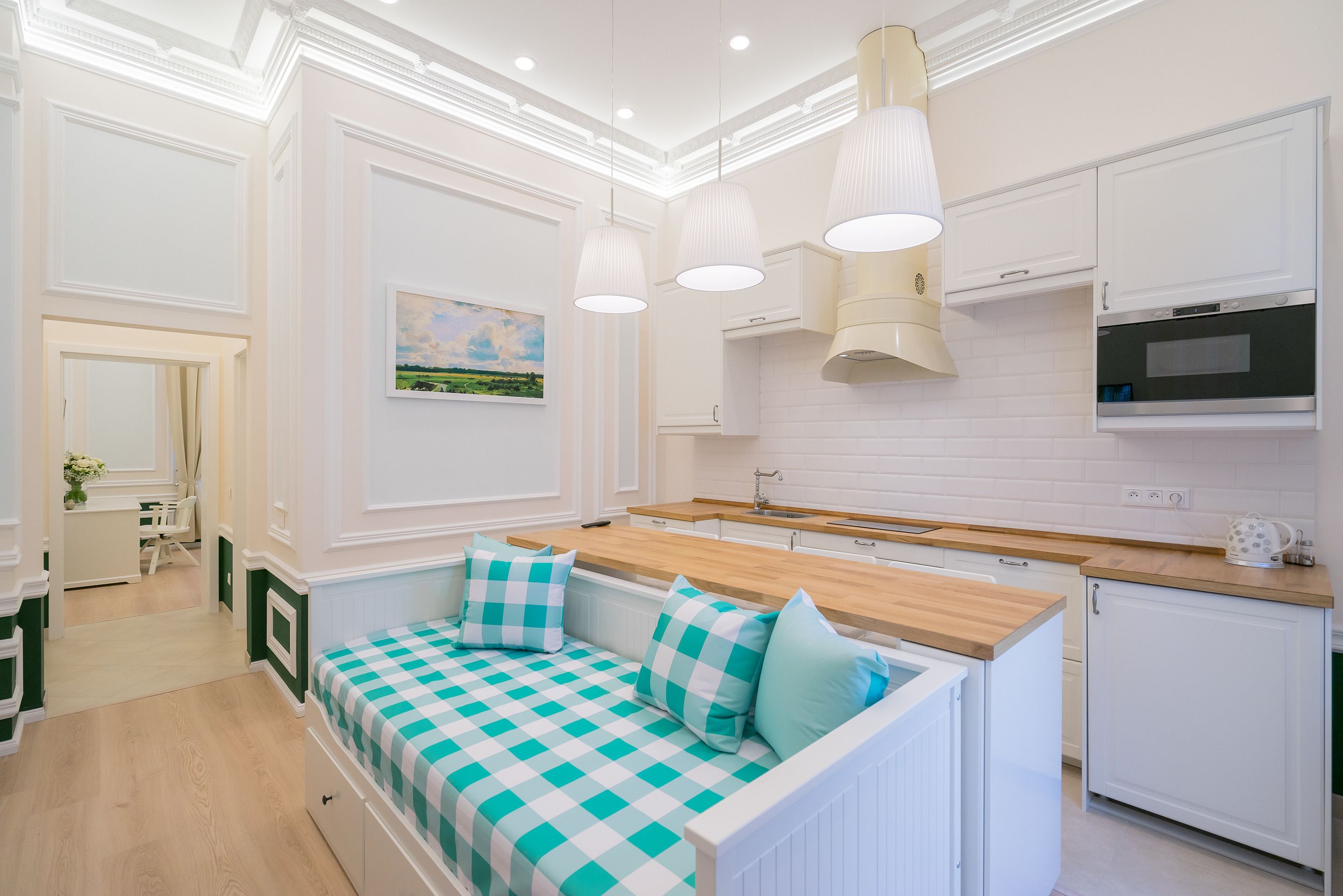 A modern kitchen with white cabinetry, a wooden countertop, and a built-in oven. There is a seating area with a checkered bench and cushions.