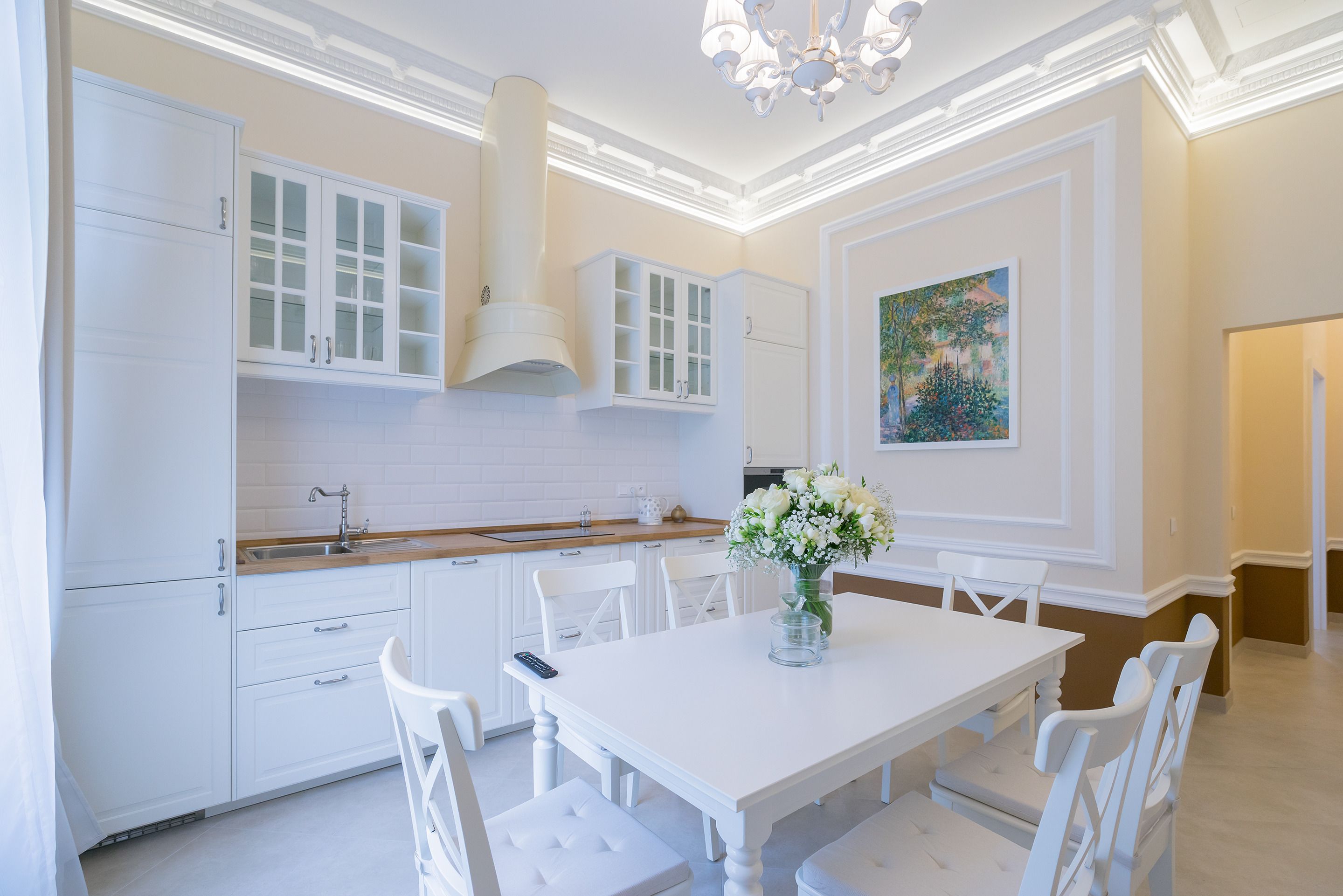 A modern kitchen with white cabinetry, a central island, and a dining area with white chairs.