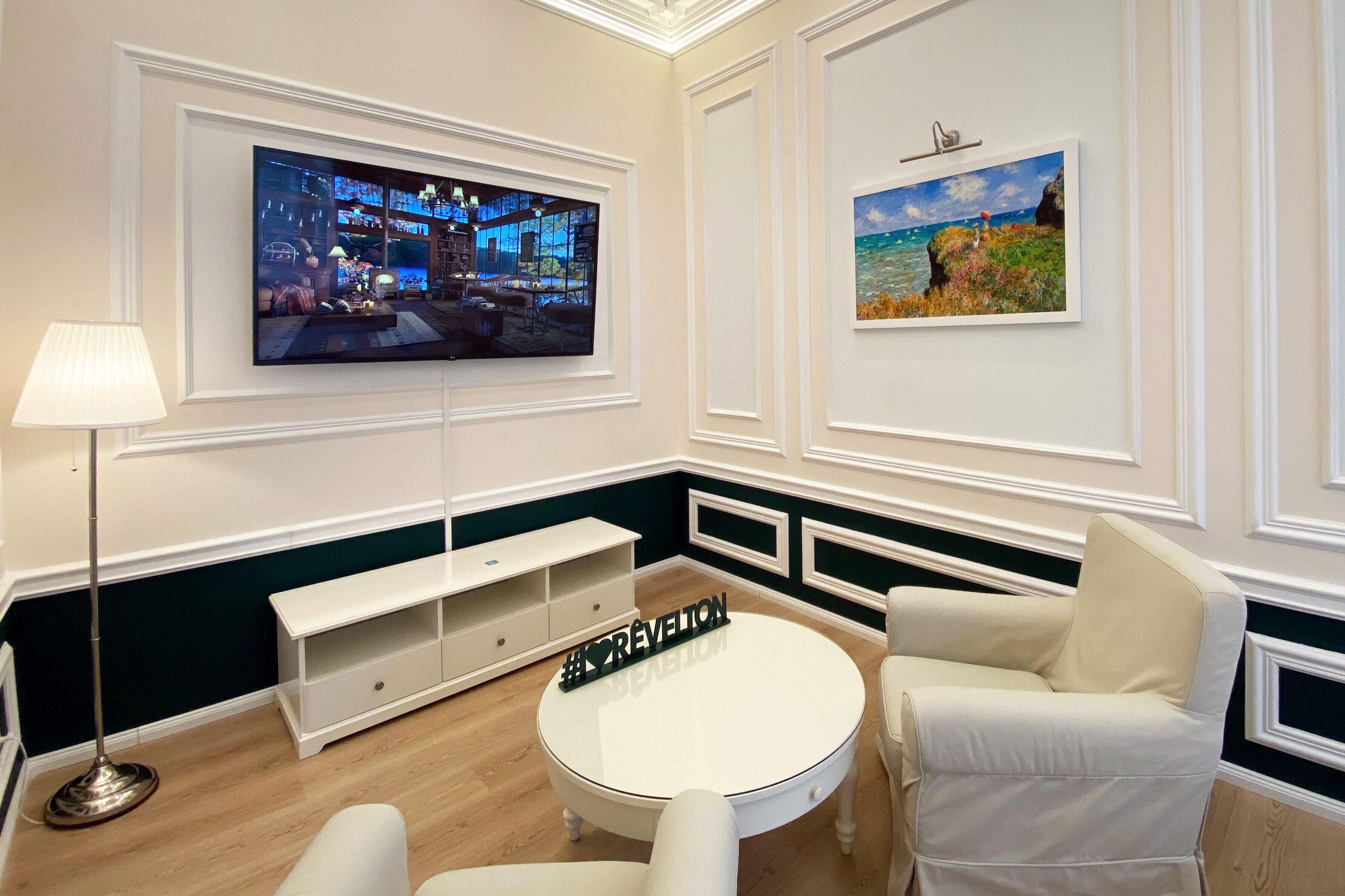 Un salon moderne avec un téléviseur à écran plat, une table basse ronde et deux fauteuils blancs.