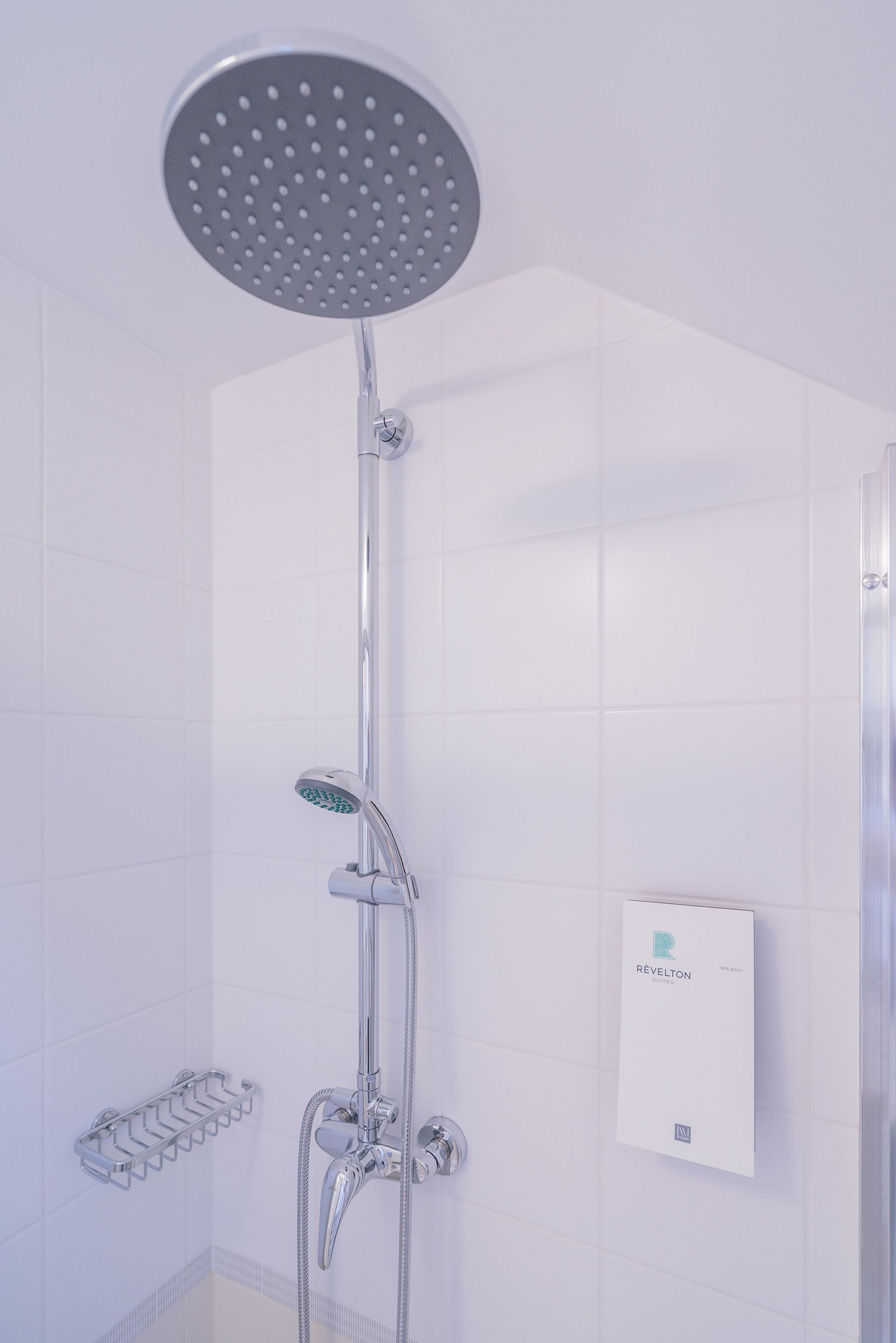 A modern shower with a rain showerhead, handheld showerhead, and a control panel.