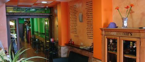 A hotel lobby with a reception desk, a seating area with a sofa and chairs, a display cabinet with souvenirs, and a green wall with text.