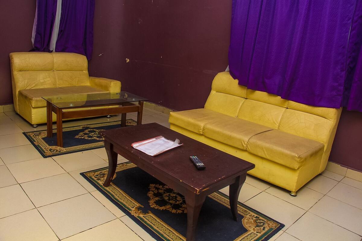 A living room with a yellow sofa, a glass coffee table, and a wooden table with a remote control.