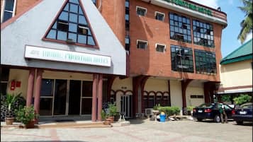 Welcome to the Divine Fountain Hotel, featuring a striking triangular design element and a warm, inviting entrance with potted plants and outdoor seating.