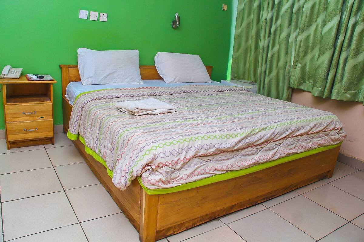 A bedroom with a wooden bed, a bedside table with a phone, and a green wall.