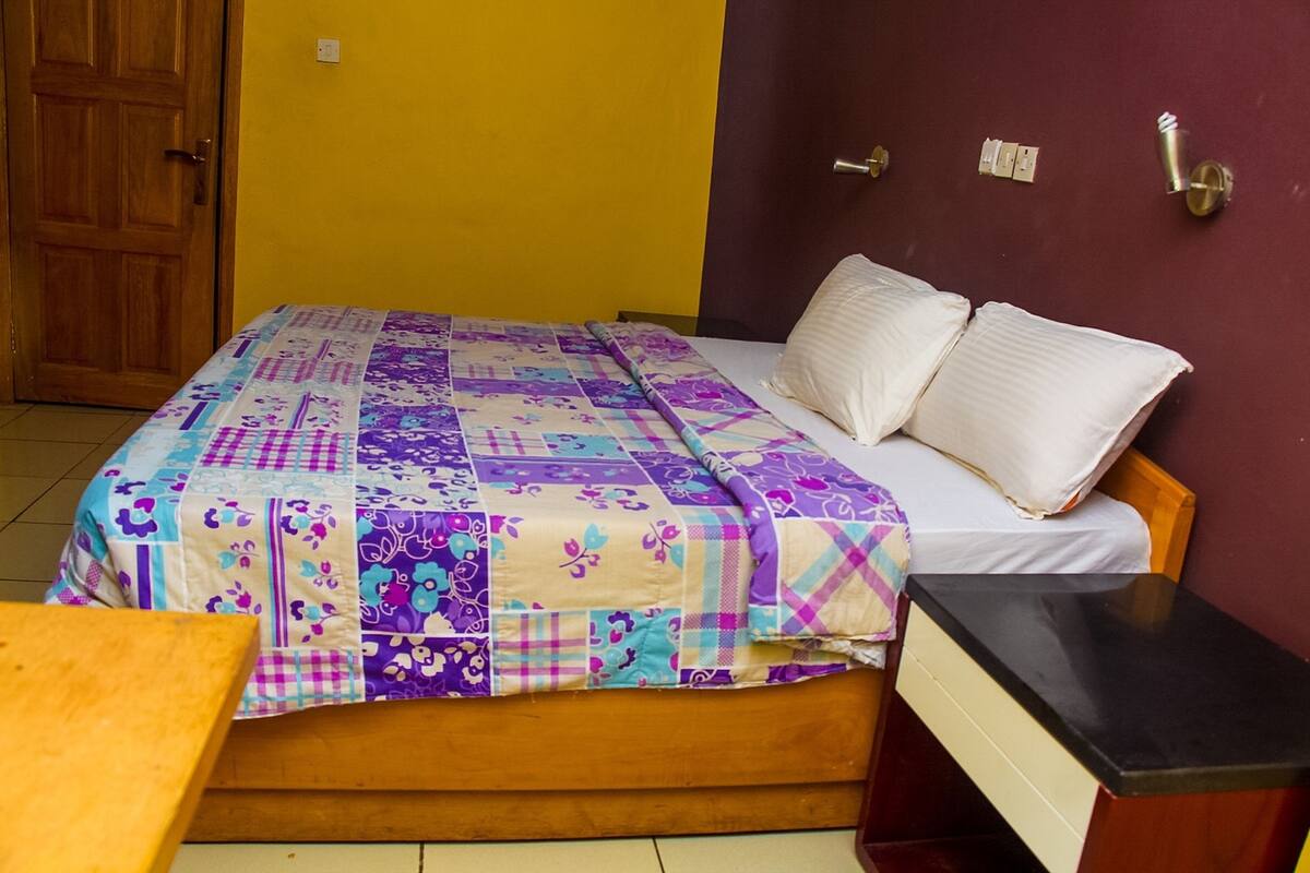 A room with a bed, a nightstand, a wooden table, and a door.