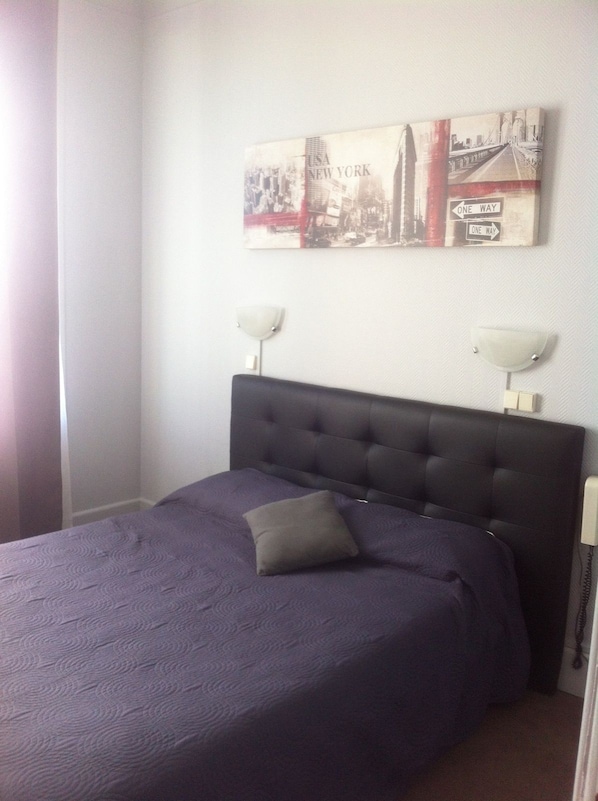 Ein Hotelzimmer mit einem großen Bett, einem Kopfteil, zwei Nachttischlampen und einem Wandbild, das eine Stadtansicht zeigt.
