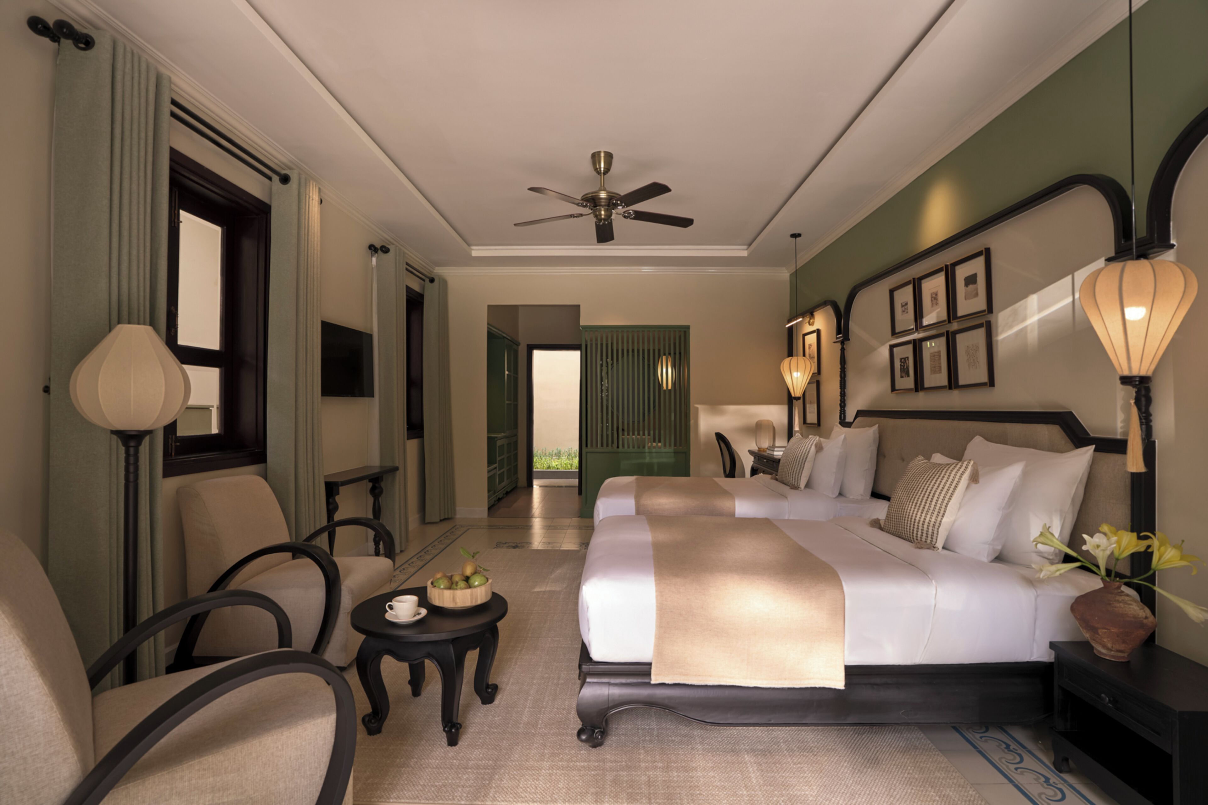 A hotel room with a bed, seating area, ceiling fan, and a view through an open door.