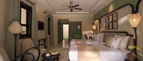 A hotel room with a bed, seating area, ceiling fan, and a view through an open door.
