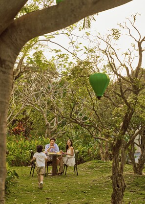 A group of people dining outdoors with trees and greenery in the background. - Grand Signature Resort Hoi An by M Village, a brand of Modern Village Lifestyle (Da Nang)
