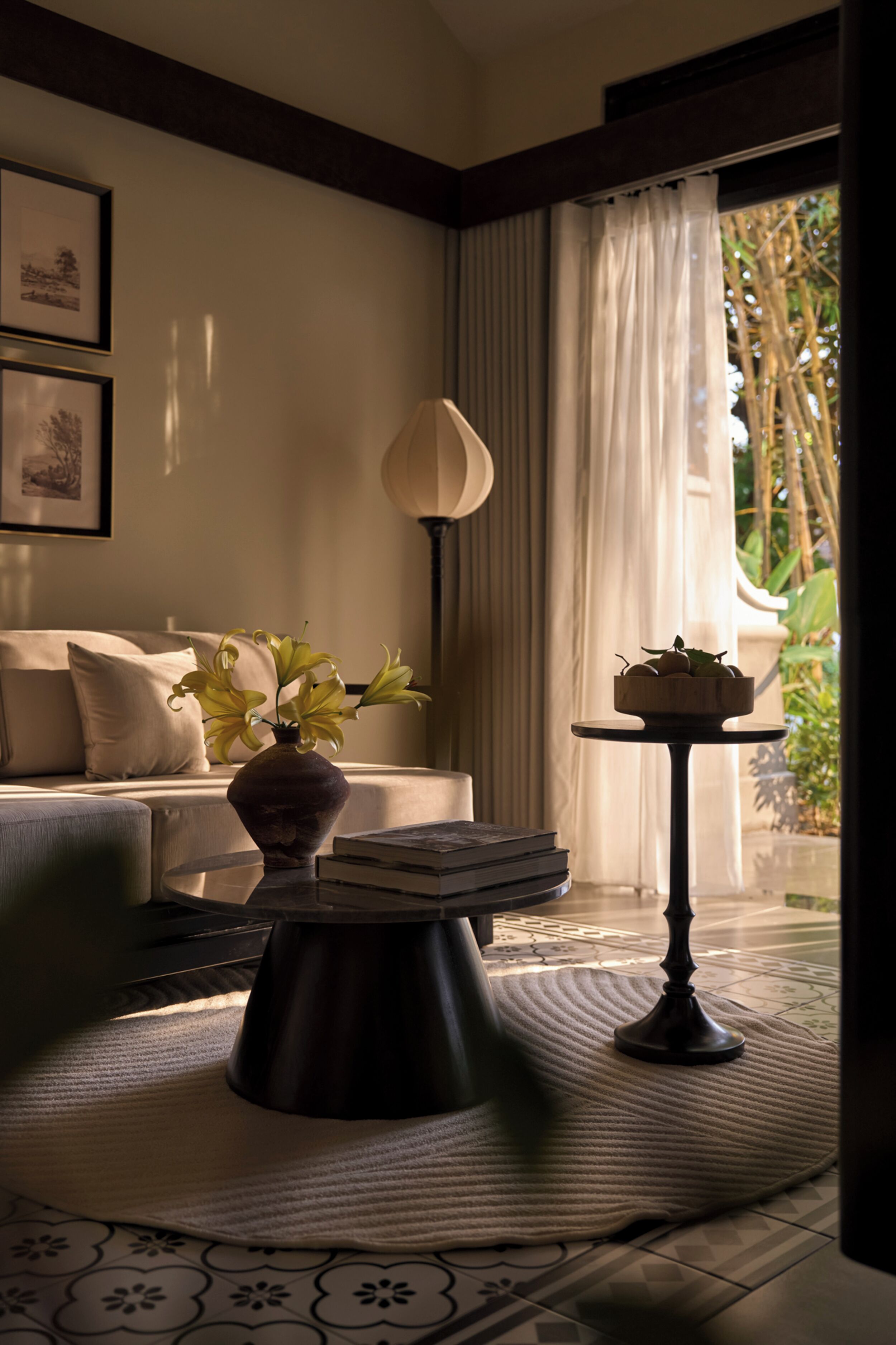 Ein Wohnzimmer mit einer Couch, einer Vase mit Blumen, einem Tisch mit Büchern und Blick ins Grüne.