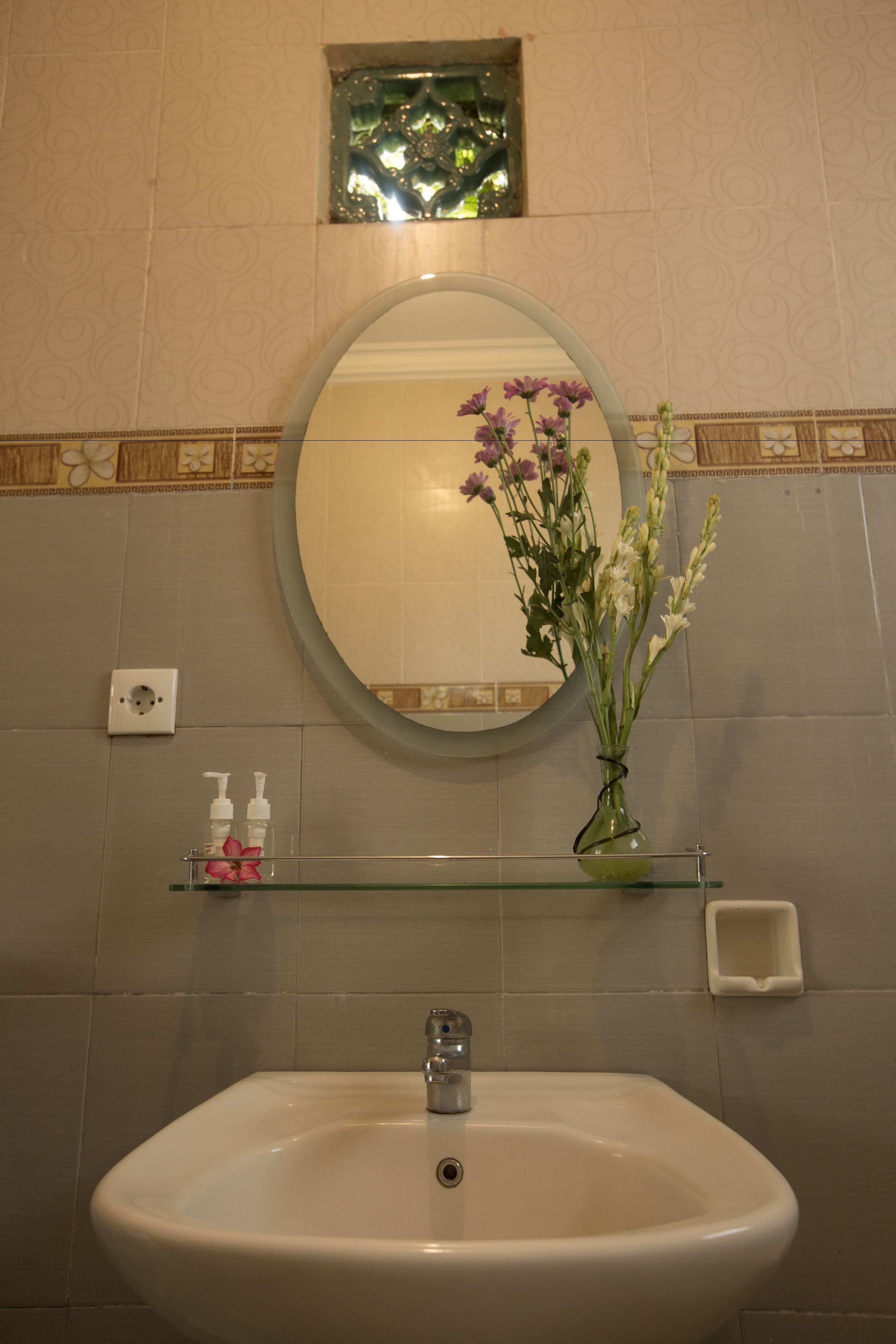 A bathroom with a sink, mirror, and a vase with flowers.
