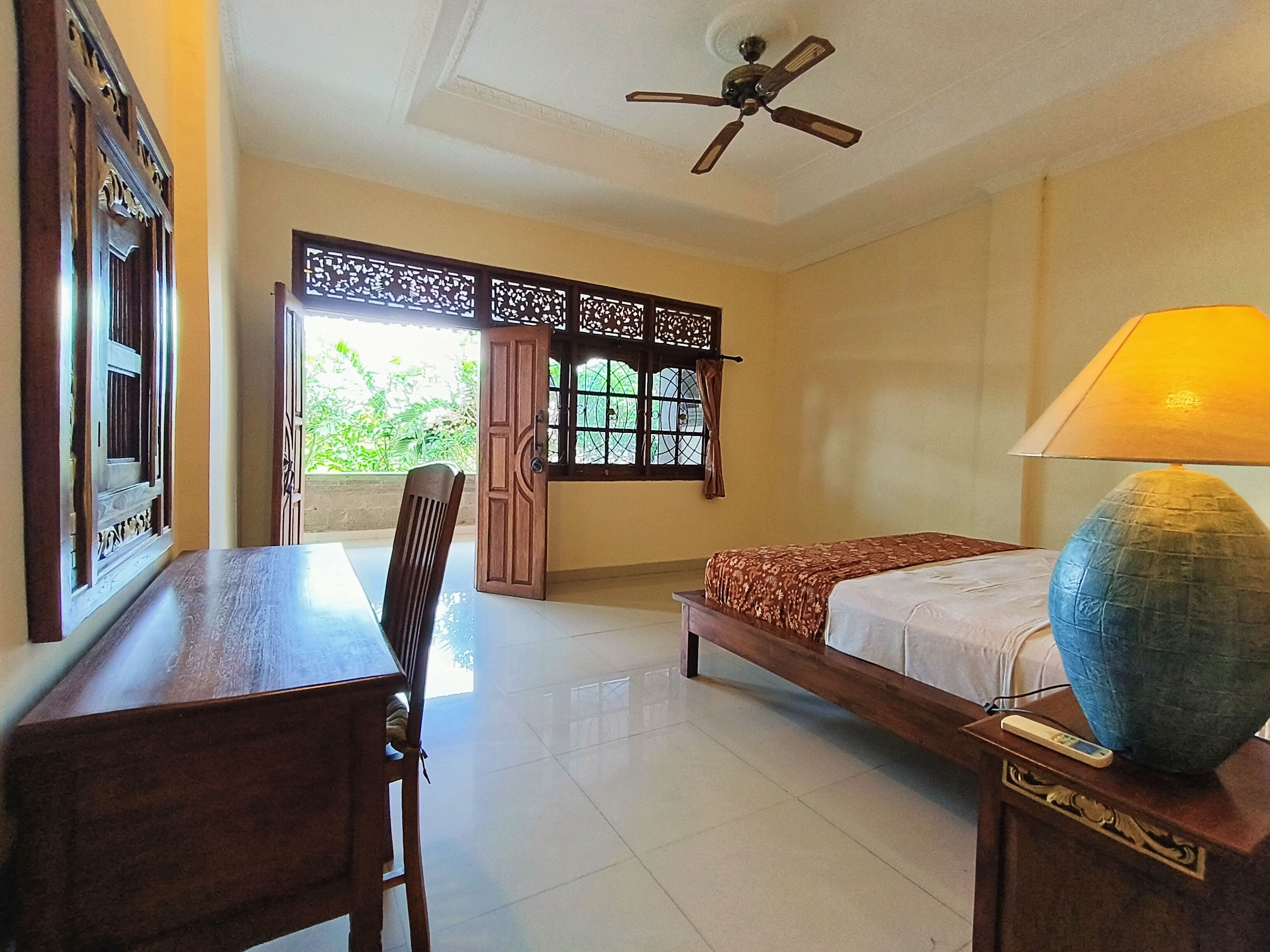 A room with a bed, a desk, a chair, a ceiling fan, and a window with decorative shutters.