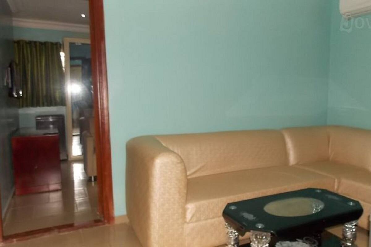 A living room with a beige sofa, a small table, and a mirror. There is a door leading to another room.