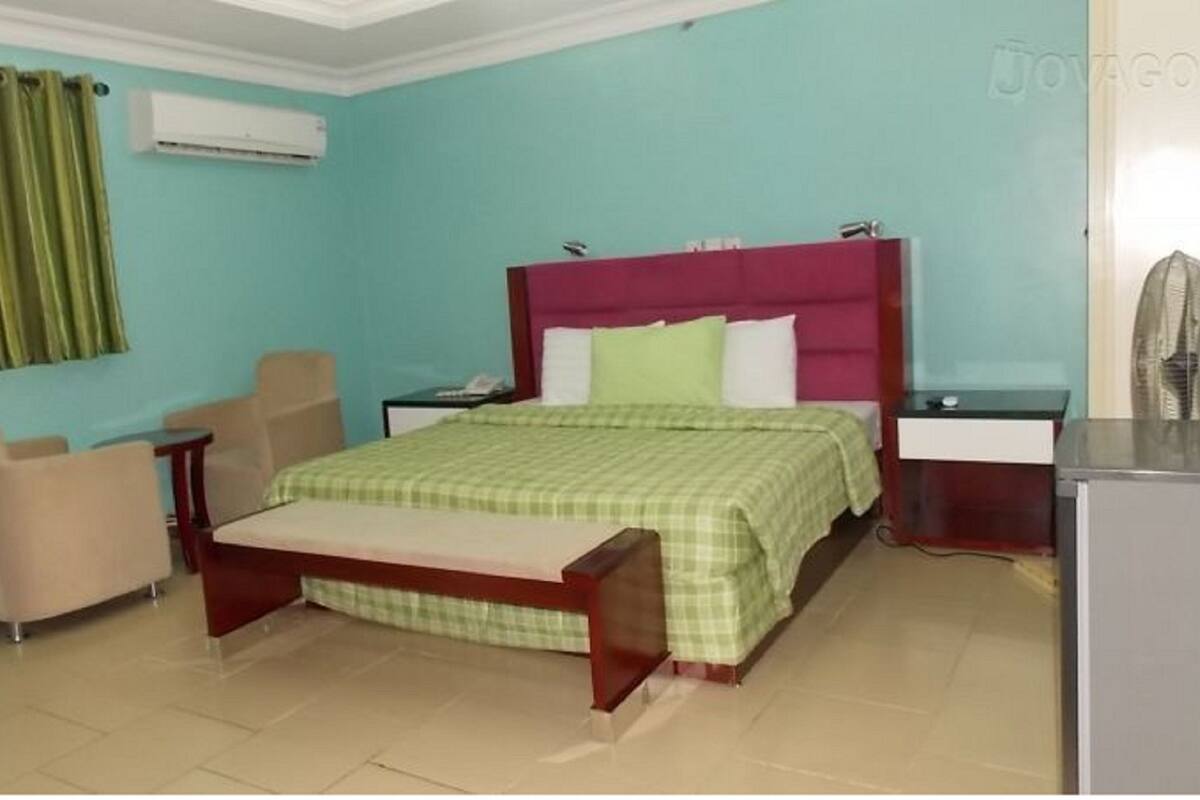 A bedroom with a bed, a desk, a chair, a wardrobe, and an air conditioning unit.