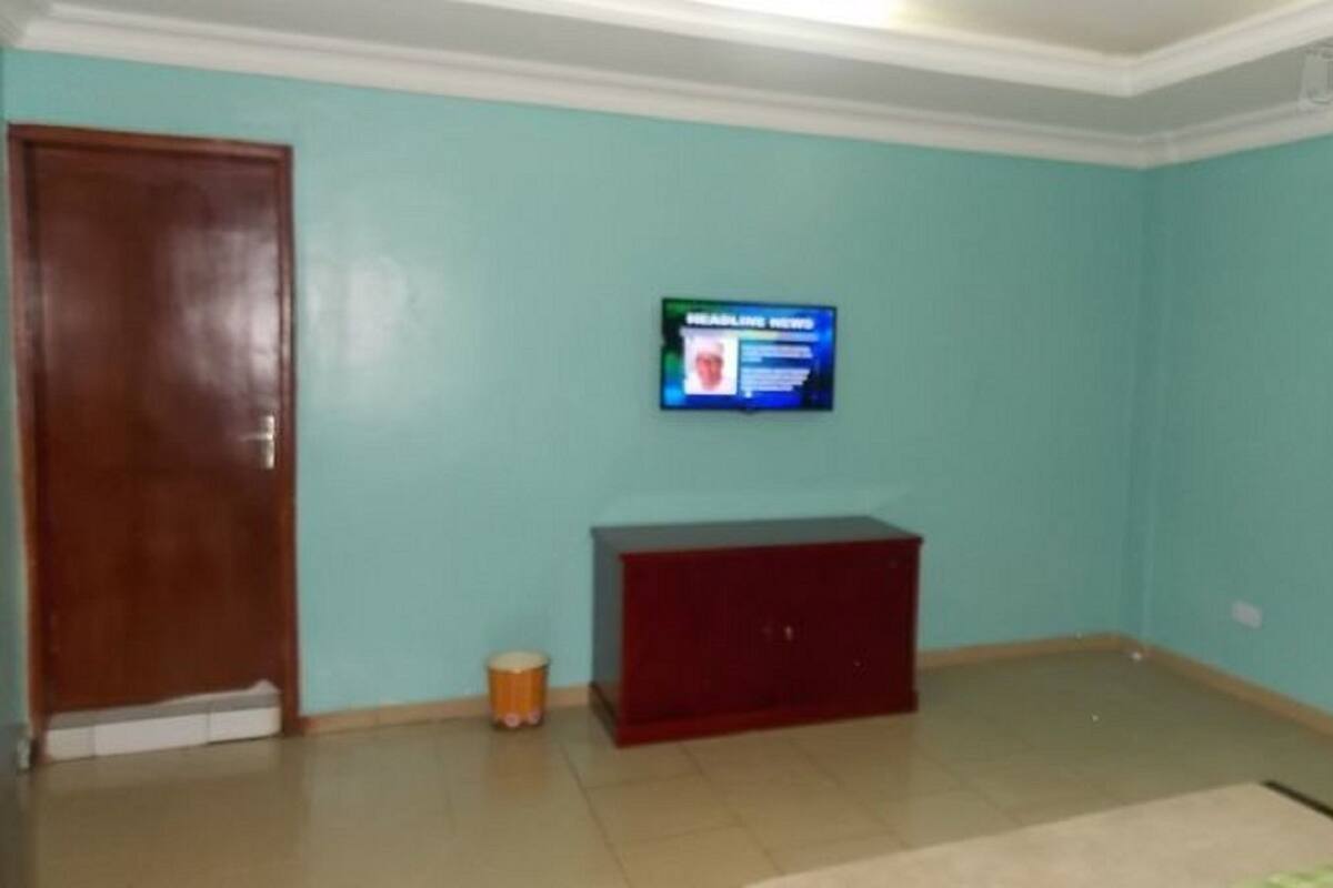 A room with teal walls, a wooden door, a small red cabinet, and a television mounted on the wall.