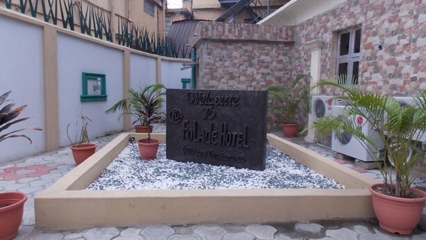 A welcome sign for Folade Hotel, surrounded by potted plants and a gravel area. - Divine Foutain Apapa Branch (Lagos)
