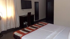 A hotel room with a bed, a desk, a chair, a TV, and a door. - Divine Fountain Agidingbi (Lagos)