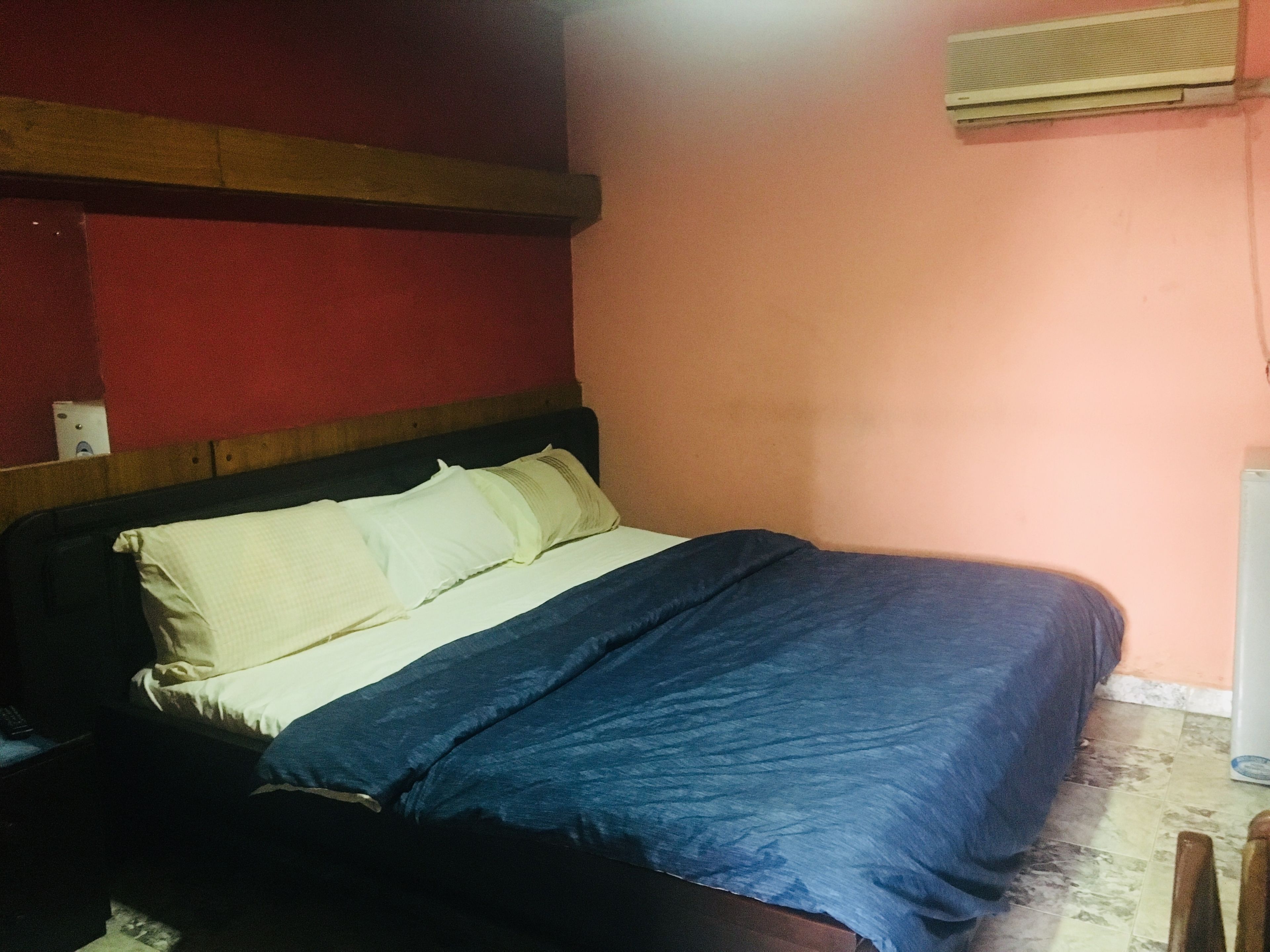 A bedroom with a bed, a wooden headboard, a wall-mounted air conditioner, and a red wall.