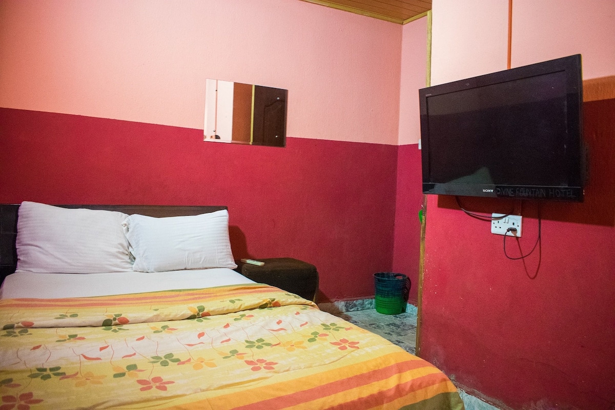 A hotel room with a bed, a television mounted on the wall, and a small trash bin.