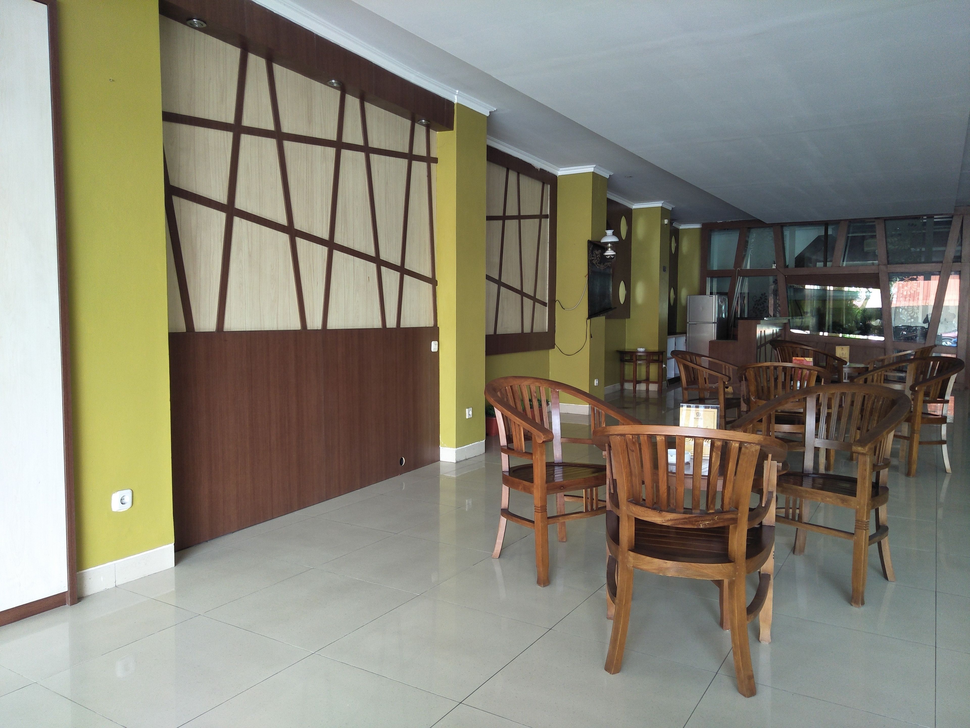 Un comedor con sillas de madera y una mesa, una cocina con refrigerador, y un ventanal que proporciona luz natural.