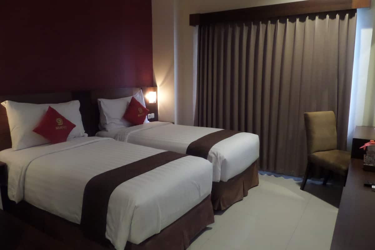 Une chambre d’hôtel avec deux lits, une chaise, un bureau et un rideau.