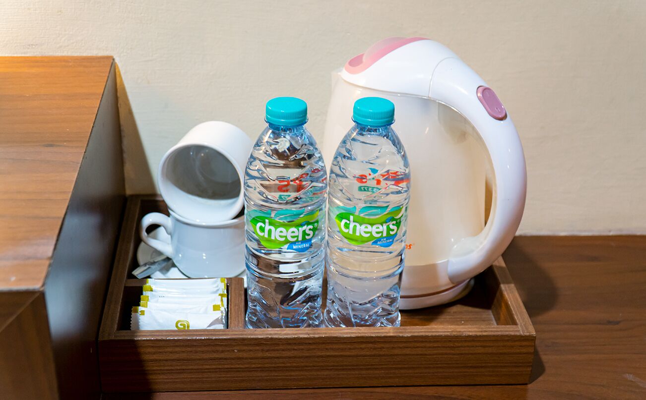 Una bandeja de madera con una taza blanca, dos botellas de agua mineral Cheers y una tetera eléctrica blanca.