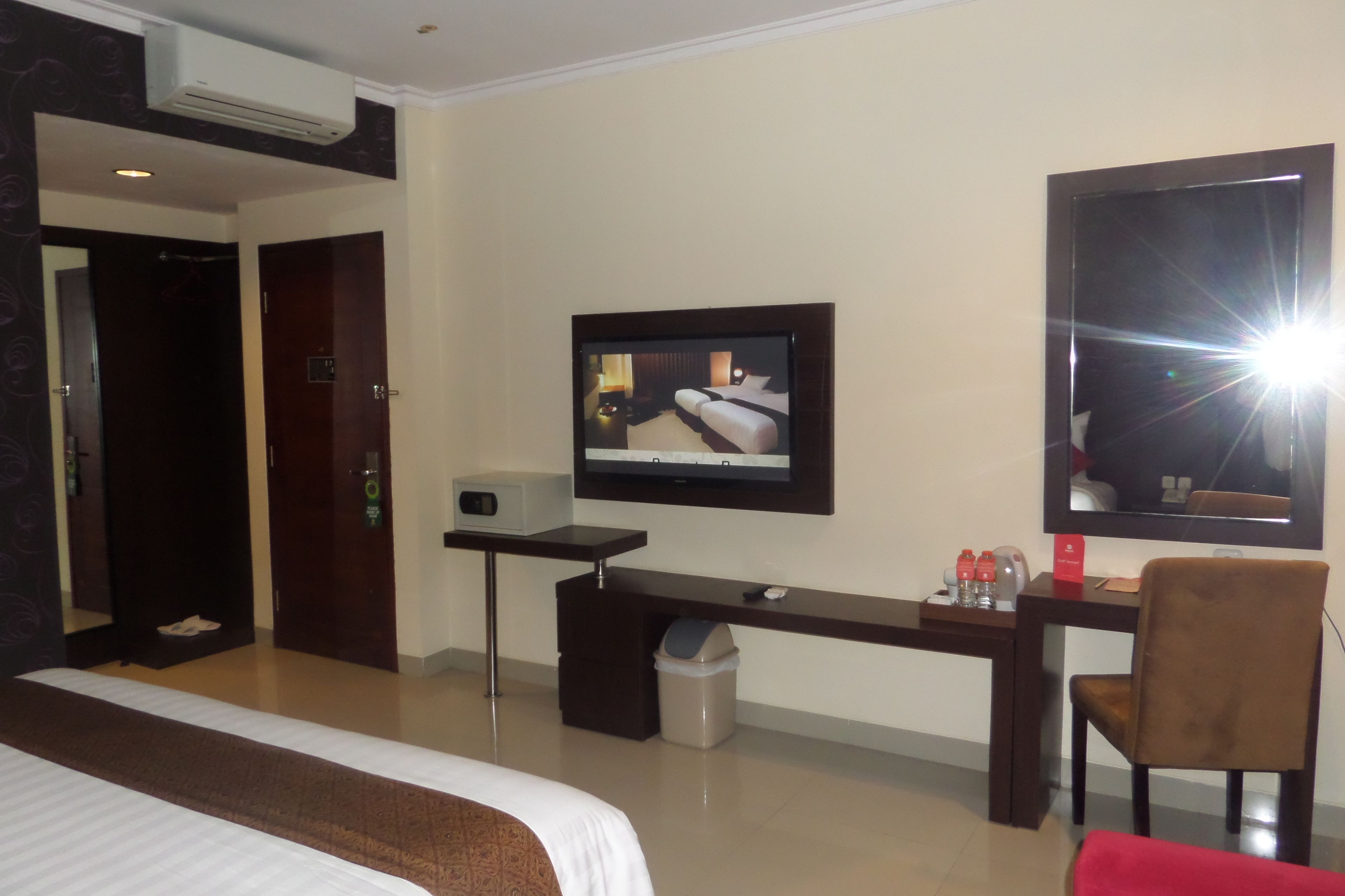 A hotel room with a bed, a desk with a computer, a chair, a TV, and a mirror.