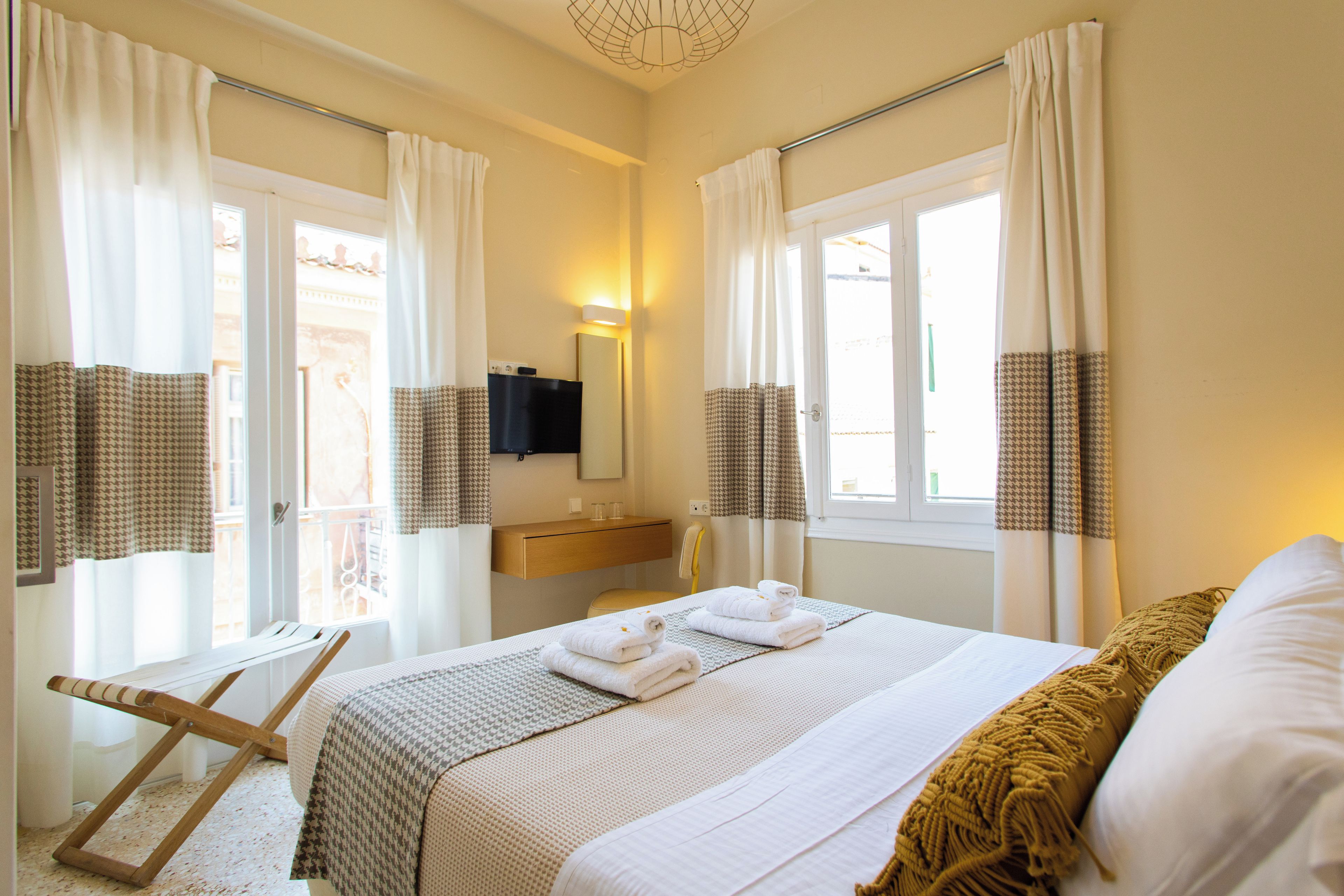 Une chambre d’hôtel avec un lit, un banc, une télévision et une fenêtre avec des rideaux.