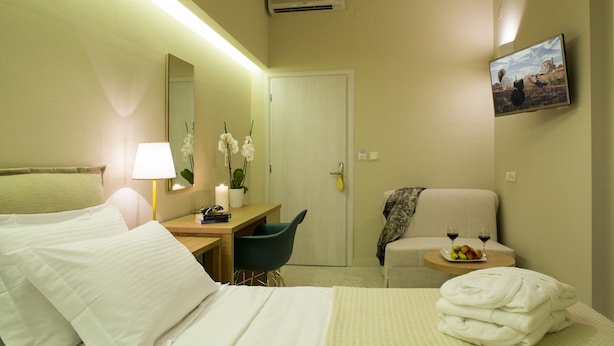Une chambre d’hôtel comprenant un lit, un bureau, une chaise, une petite table avec une assiette de fruits et des verres, ainsi qu’un téléviseur fixé au mur.