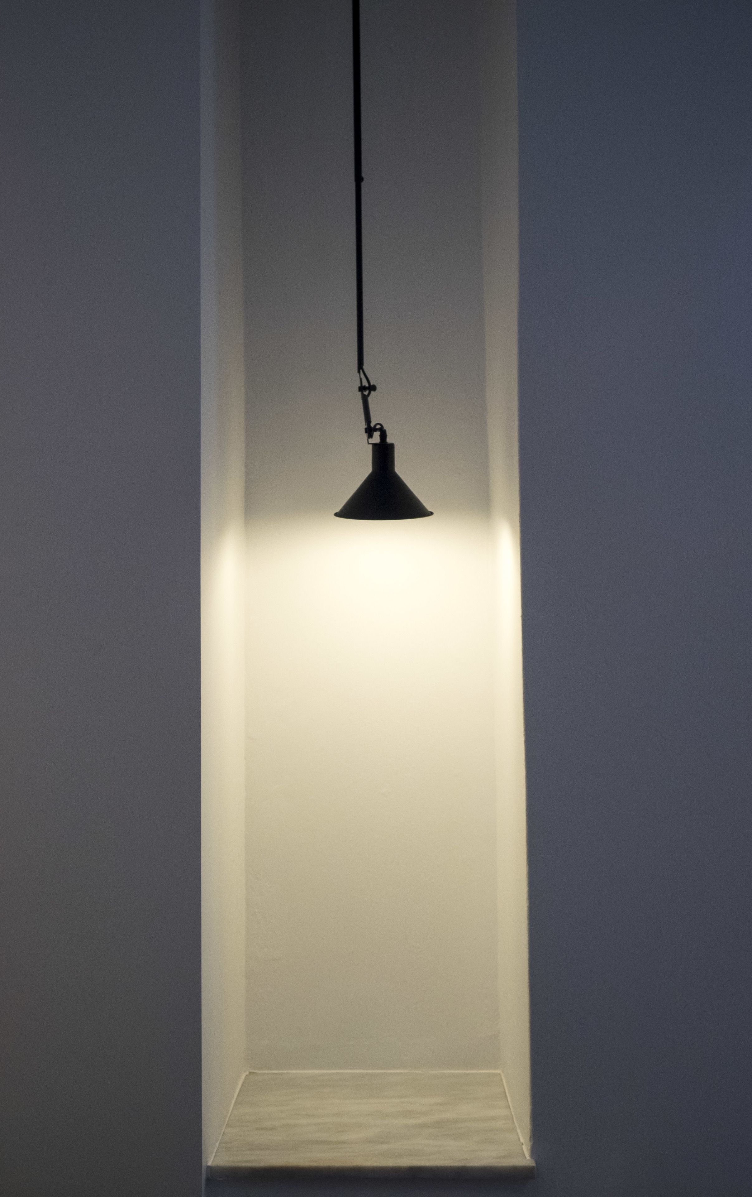 A pendant light fixture hanging from the ceiling in a room with plain walls.