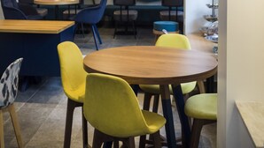 Un espace de restauration moderne avec des tables rondes, des chaises colorées et des luminaires suspendus.