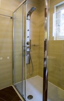 Ducha envuelta en vidrio con cabezal de ducha manual, grifo empotrado y panel de control.