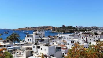 Un pueblo costero con edificios blancos, un mar azul cristalino y una fortaleza histórica en una colina.