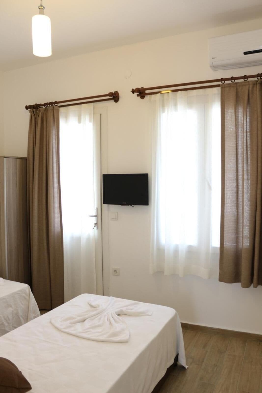 A hotel room with two beds, a TV mounted on the wall, and an air conditioning unit.