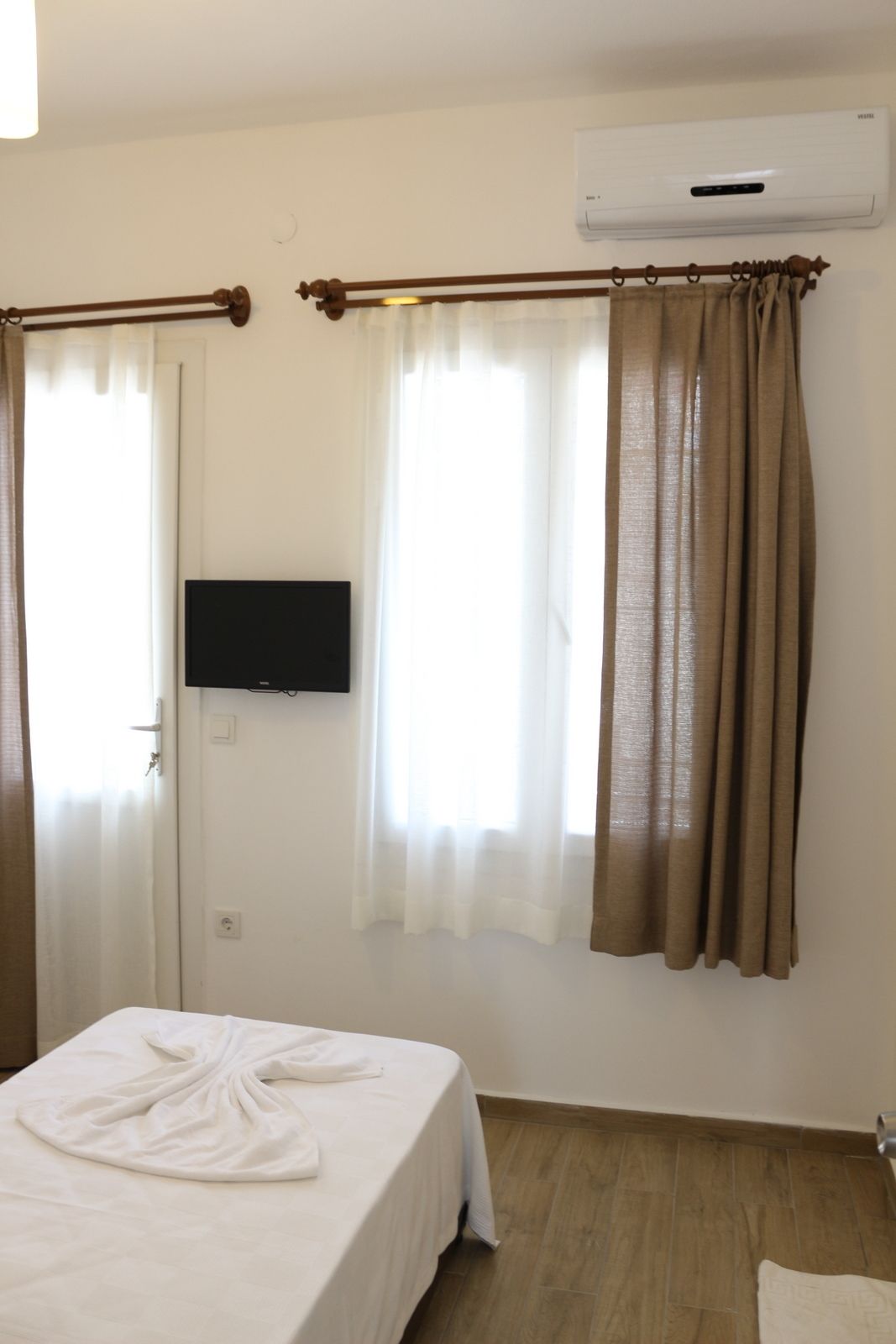 A hotel room with a bed, a TV mounted on the wall, and an air conditioning unit.