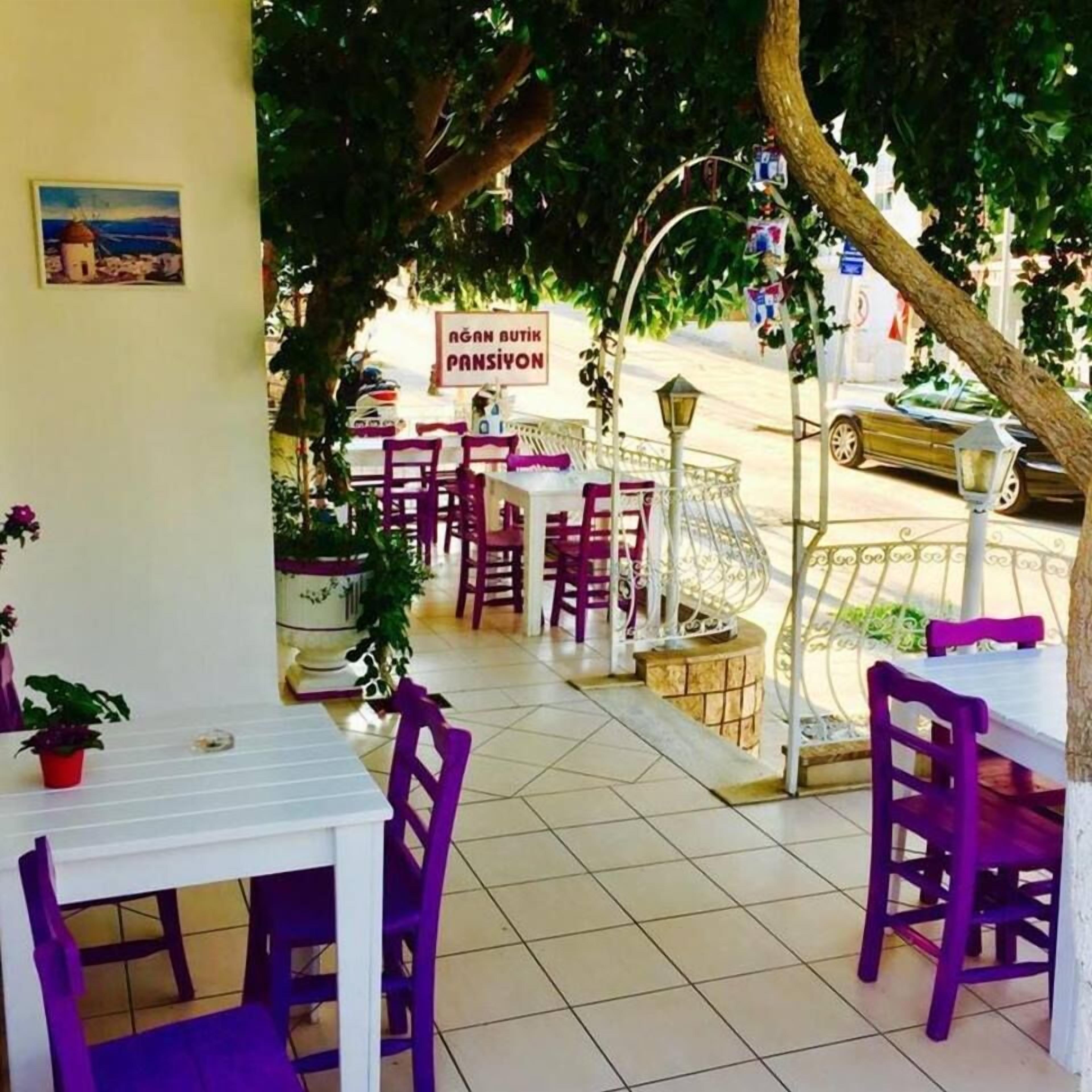 An outdoor cafe with tables and chairs, a street view, and a sign reading "AGAN BUTIK PANSIYON".